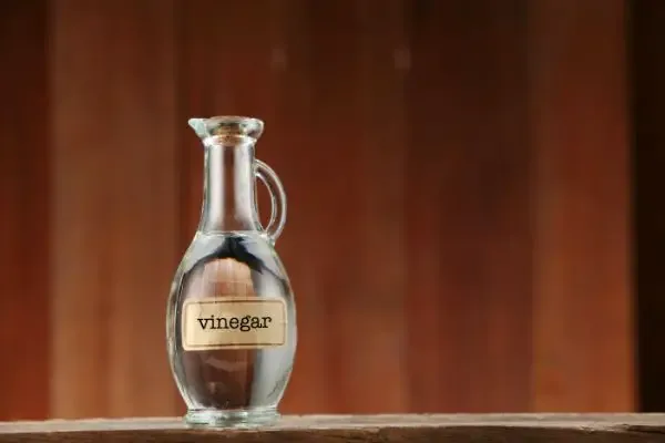 White vinegar in a glass bottle on a wooden counter.