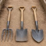 Garden fork, spade, and shovel arranged side by side on a garden path.